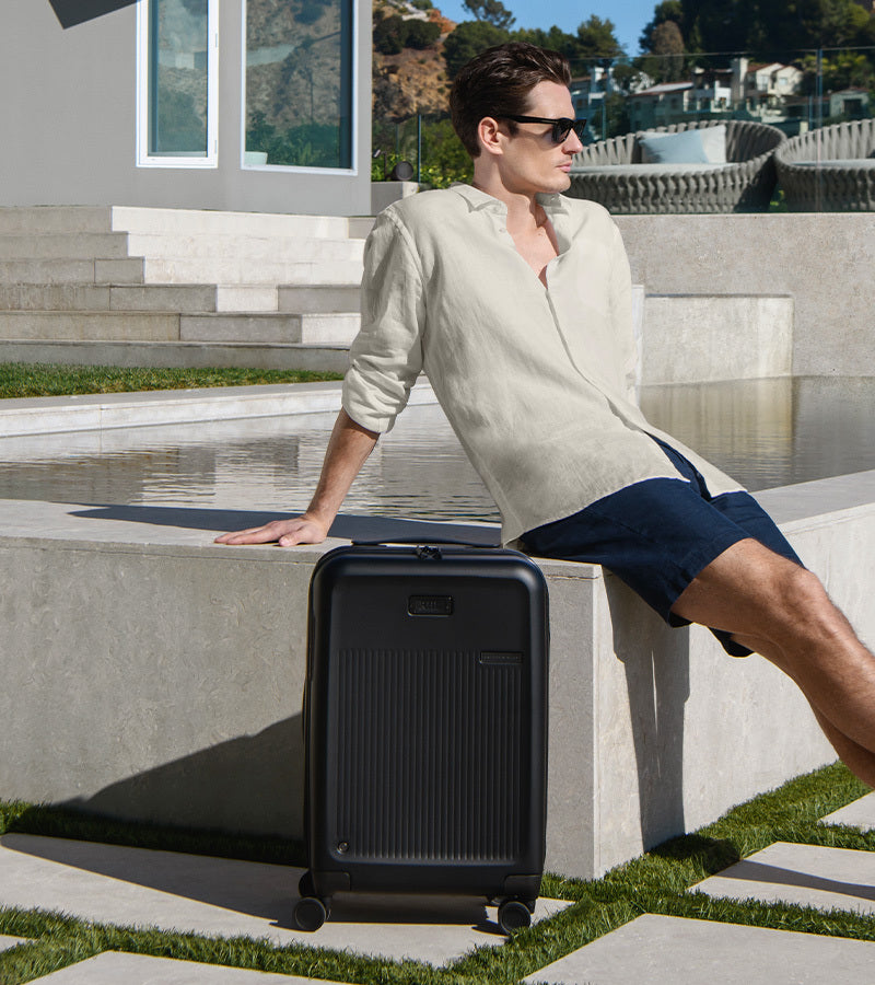 Man sitting on steps with a black suitcase next to him, wearing sunglasses and a light-colored shirt.